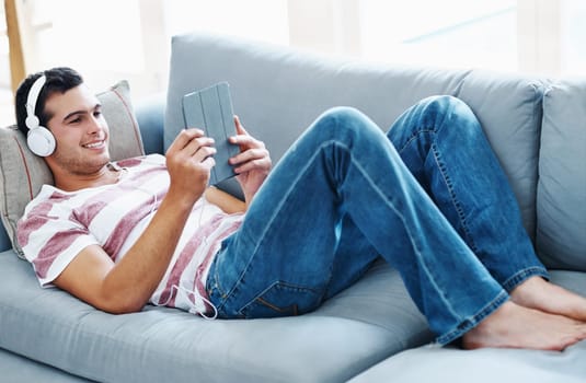 Smile, headphones and man with tablet on sofa for online streaming, video and watching movie. Happy, relax and male person with technology at home for network, connectivity or subscription on weekend.