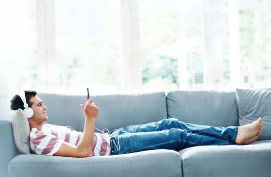 Man, headphones and phone on sofa in house for music, streaming and self care while on study break. Guy, headset and tech on couch in home living room for social media, video and app or radio.