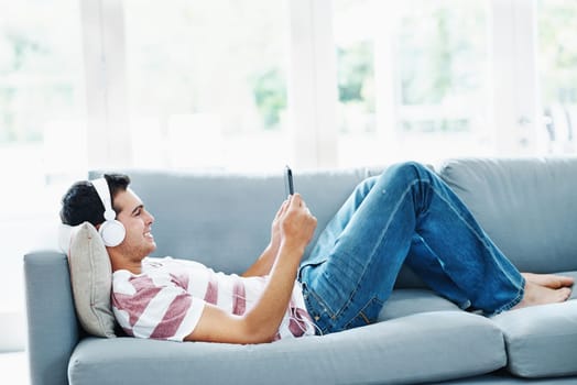 Male person, headphones and phone on sofa in house for music, streaming and self care while on study break. Man, headset and tech on couch in home living room for social media, video and app or radio.