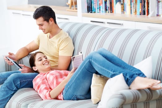 Couple, home and happy with bonding on sofa with tablet for social media, networking and entertainment. People, couch and living room with reading book or novel for fiction, story and fun to relax.