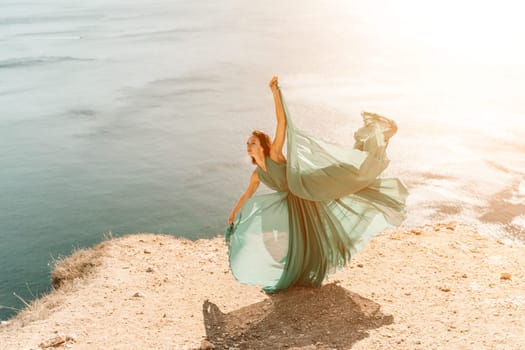 Woman green dress sea. Female dancer posing on a rocky outcrop high above the sea. Girl on the nature on blue sky background. Fashion photo