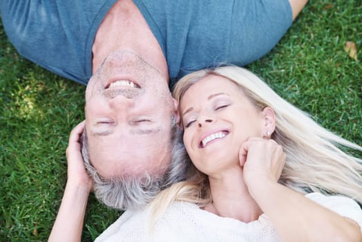Mature, happy couple and outdoor relax on grass from above for marriage anniversary, travel or relationship. Man, woman and top view in garden park in New Zealand for holiday trip, peace or nature.