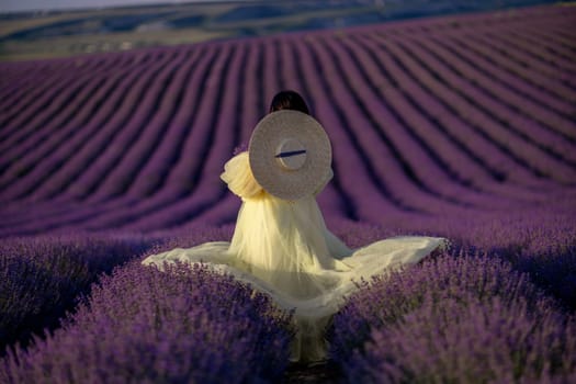 Woman lavender field sunset. Back view woman in yellow dress and hat. Aromatherapy concept, lavender oil, photo session in lavender.