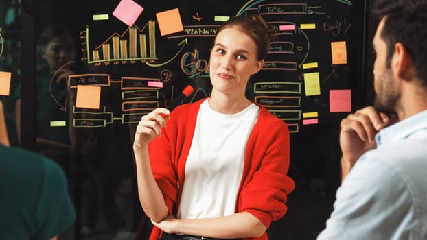 Closeup of young beautiful project manager present graph and business plan on glass wall. Skilled businesswoman show marketing strategy. Leader sharing brainstorming ideas to investor. Tracery