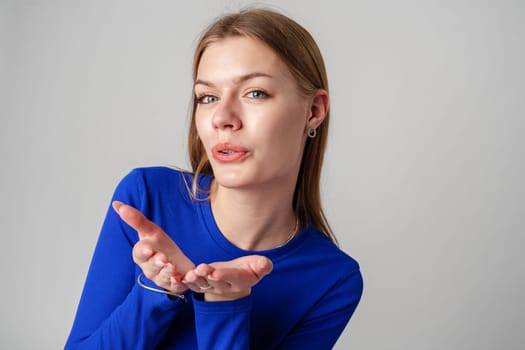 Young Woman in Blue Top Blowing a Kiss Against a Neutral Background.close up