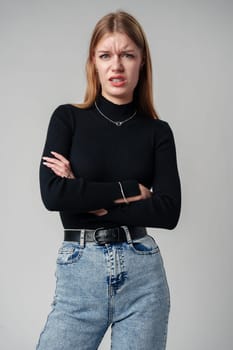 Young Woman In Black Shirt Expressing Discontent Against Grey Background close up