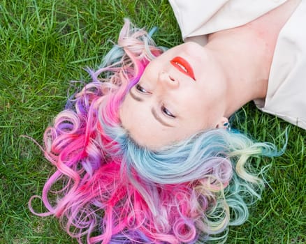 Top view of Caucasian woman with multi-colored hair lying on green grass