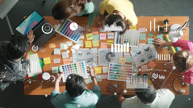 Top down view of business team with casual outfit looking laptop screen and sharing idea. Aerial view of manager works and checking color palette at table with statistic graph holographic. Symposium.