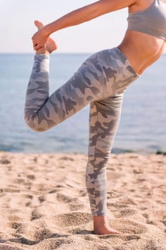 cutout detail of the legs of woman in sportswear exercising on the beach with yoga poses, concept of mental relaxation and healthy lifestyle