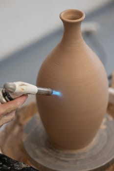 Close-up of a potter's hands firing a jug with a gas burner on a potter's wheel. Vertical photo