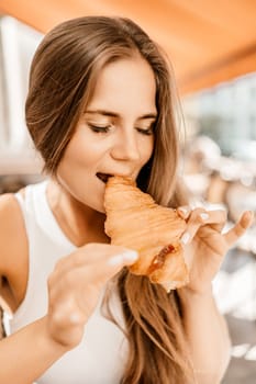 A woman is eating a croissant. The croissant is half eaten and has a jelly filling