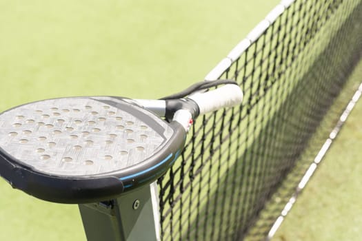 Padel racket and padel ball on a green court in the sunset. High quality photo