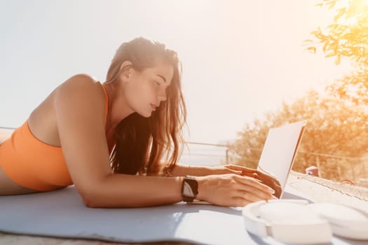 Digital nomad, Business woman working on laptop by the sea. Pretty lady typing on computer by the sea at sunset, makes a business transaction online from a distance. Freelance, remote work on vacation