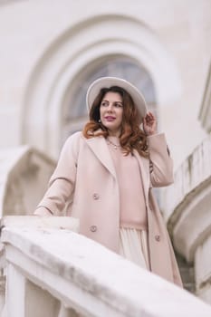 woman in elegant coat and hat against an intricate architectural backdrop, harmoniously blending modern fashion with historical allure. The soft daylight adds to its timeless appeal