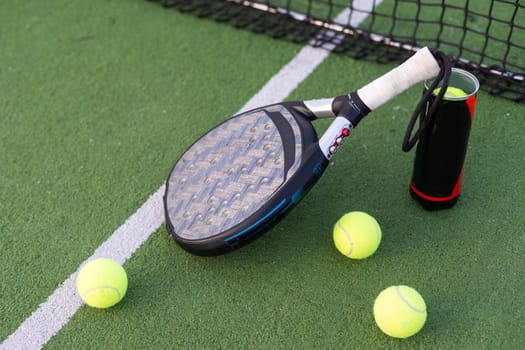 Blue padel racket and yellow balls placed on court near net on sunny day. High quality photo