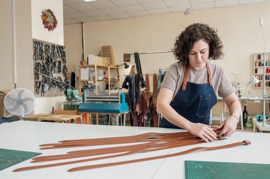 Caucasian woman makes belts from genuine leather in a workshop