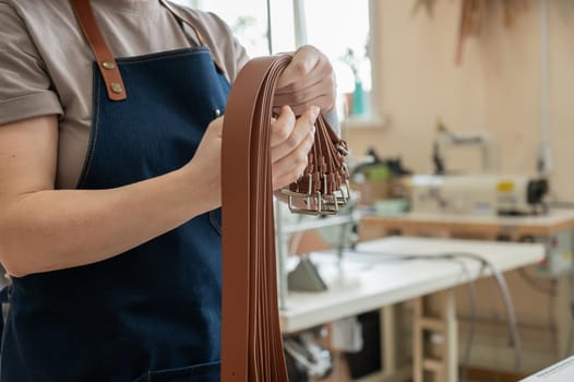 Close-up of a Caucasian woman's hands making genuine leather belts in a workshop