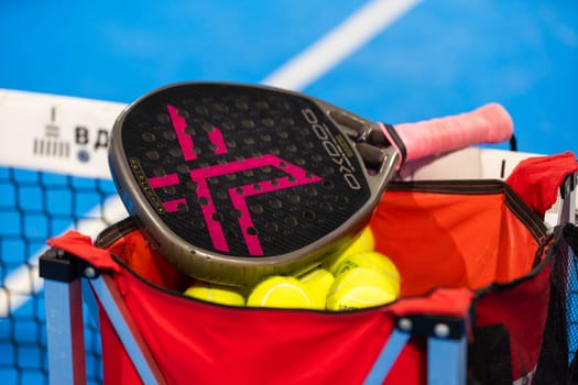 Kyiv, Ukraine, April 18, 2024. Black professional paddle tennis racket and ball with natural lighting on blue background. Horizontal sport theme poster, greeting cards, headers, website and app. High quality photo
