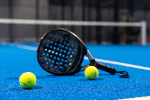 Kyiv, Ukraine, April 18, 2024. Black professional paddle tennis racket and ball with natural lighting on blue background. Horizontal sport theme poster, greeting cards, headers, website and app. High quality photo