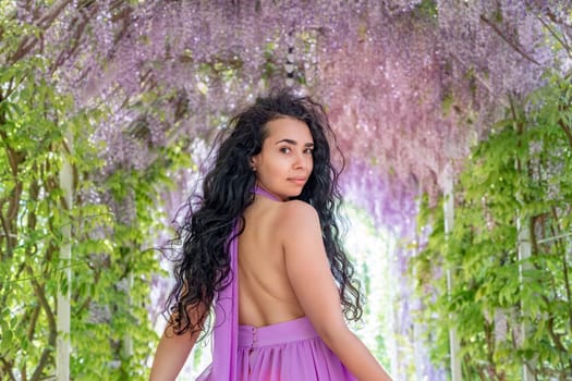 Woman wisteria lilac dress. Thoughtful happy mature woman in purple dress surrounded by chinese wisteria.