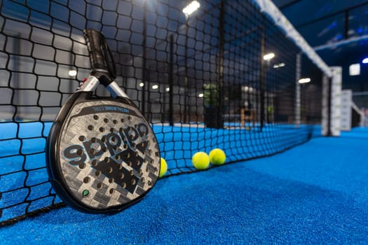 Kyiv, Ukraine, April 18, 2024. Black professional paddle tennis racket and ball with natural lighting on blue background. Horizontal sport theme poster, greeting cards, headers, website and app. High quality photo