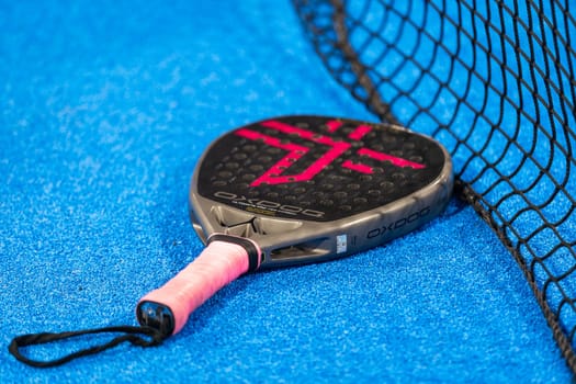 Kyiv, Ukraine, April 18, 2024. Black professional paddle tennis racket and ball with natural lighting on blue background. Horizontal sport theme poster, greeting cards, headers, website and app. High quality photo