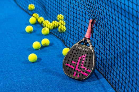 Kyiv, Ukraine, April 18, 2024. Black professional paddle tennis racket and ball with natural lighting on blue background. Horizontal sport theme poster, greeting cards, headers, website and app. High quality photo