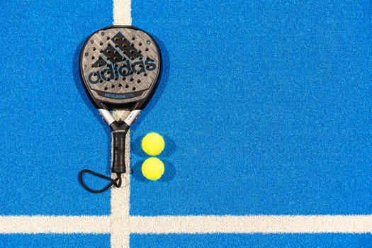 Kyiv, Ukraine, April 18, 2024. Black professional paddle tennis racket and ball with natural lighting on blue background. Horizontal sport theme poster, greeting cards, headers, website and app. High quality photo