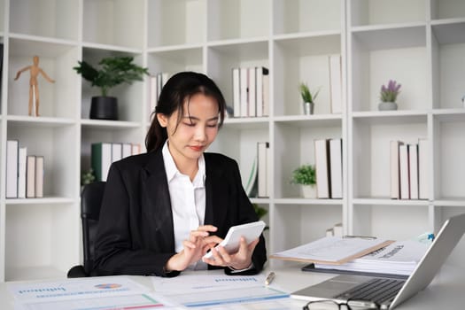 Asian female accountant Use a calculator to calculate business numbers on a white wooden table in the office..