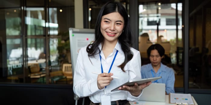 Young Asian business woman entrepreneur standing in office holding digital tablet. Businesswoman leader employee.