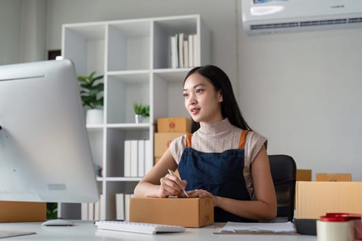 Young business woman asian working online ecommerce shopping at her shop. Young woman sell prepare parcel box of product for deliver to customer. Online selling.