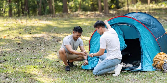 LGBTQIA Gay couple camping together in woods for holidays and helping set up a tent together.