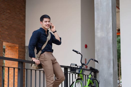 young asian businessman using mobile while walking in the street in downtown of modern city.