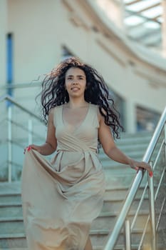 A woman in a long dress is walking up a set of stairs. She is wearing red nail polish and has a smile on her face