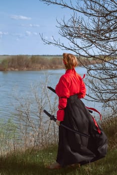 A woman with short red hair in a black and red hanfu and two katanas looks into the distance against the background of a spring river