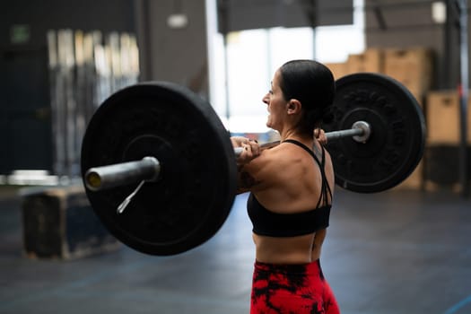 Rear view of a strong mature woman lifting weights in a gym