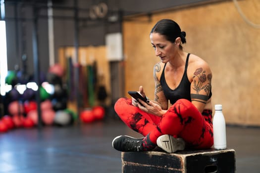 Sportive mature woman using mobile phone relaxed on a cross training gym