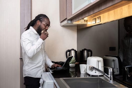 African American man using digital tablet at the kitchen reading social media internet, typing text or shopping online. Freelancer remotely working online at home.