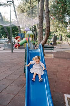 Little girl goes down the slide holding the railing. High quality photo