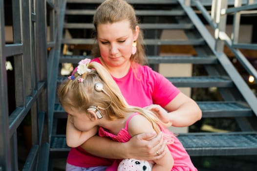 Deaf child with cochlear implant for hearing audio and aid for impairment having fun and laughs with mother outdoor in summer. Sound fitting device to help with communication listening and interaction.