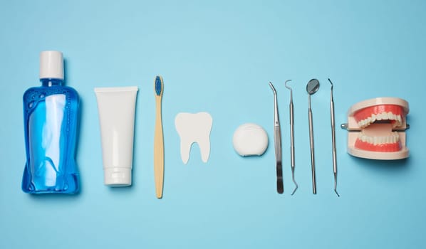 Mouthwash, toothpaste tube, dental floss and medical mirror on a blue background, oral hygiene. Top view