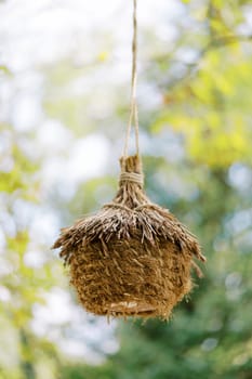 Straw nest with a roof hanging on a rope on a tree branch in the park. High quality photo