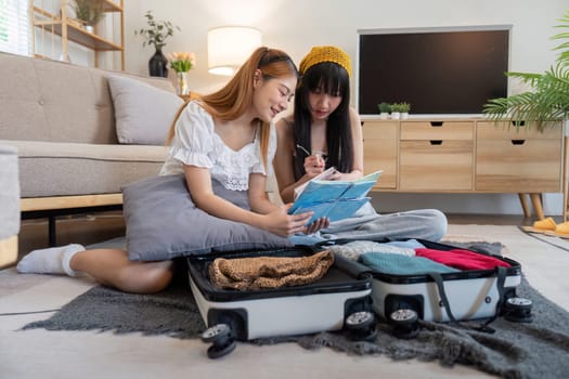 Young Asian woman packing clothes to the suitcase. Preparation for the summertime vacation. Two women are planning a trip and helping to prepare luggage to travel.