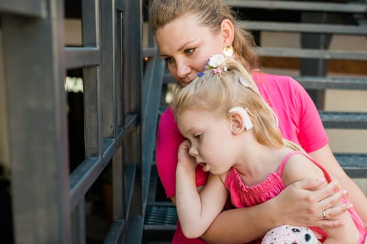 Deaf child with cochlear implant for hearing audio and aid for impairment having fun and laughs with mother outdoor in summer. Sound fitting device to help with communication listening and interaction.