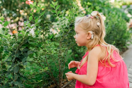 Child girl walks and have fun outdoor with cochlear implant on the head. Hearing aid and treatment concept. Copy space vertical.