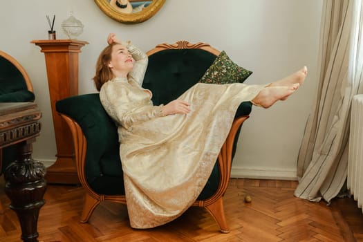 mature woman in a beautiful beige dress sits elegantly on a green armchair.