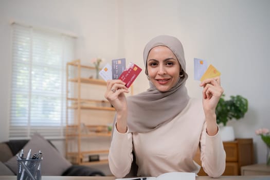 A young Muslim woman wearing a hijab sat contentedly shopping online and holding a credit card..