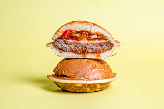 Half of burger with no top bread and a fried egg on top of the patty, isolated on a pastel yellow background.