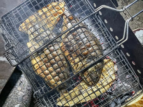 Authentic outdoor cooking scene with two grilled fishes on the grid over charcoals. Focus on the mouth-watering seafood.