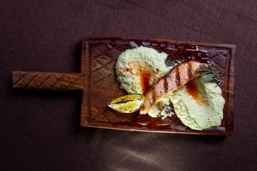 A mouthwatering grilled salmon fillet topped with a zesty lemon-herb butter sauce, presented elegantly on a rustic wooden serving board.